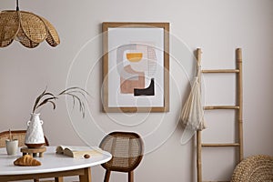 The stylish dining room with round table, rattan chair, wooden commode, pock up poster and kitchen accessories. Beige wall with