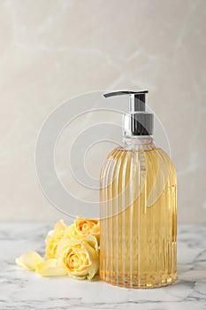 Stylish dispenser with liquid soap and beautiful flowers on white marble table
