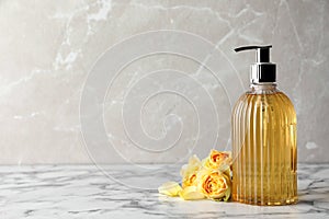 Stylish dispenser with liquid soap and beautiful flowers on white marble table, space for text