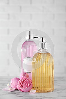 Stylish dispenser with liquid soap, bottle of shower gel and flowers on white marble table