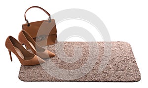 Stylish door mat with high heeled shoes and bag on white background