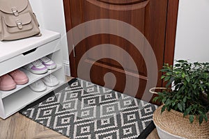 Stylish door mat, houseplant and storage with shoes in hall