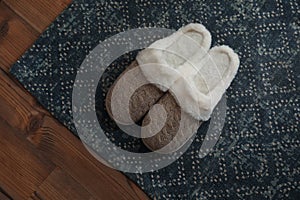 Stylish door mat and slippers on wooden floor, top view