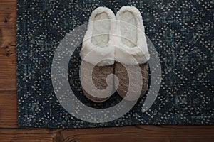Stylish door mat and slippers on wooden floor, top view