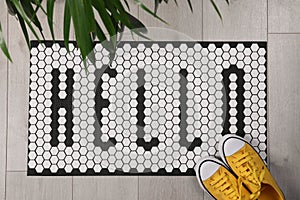 Stylish door mat with word Hello, shoes and houseplant on floor, flat lay