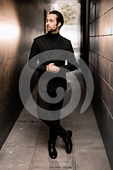 Stylish dressed businessman is walking down by stairs, looking at the side, posing for photo outdoor. Successful