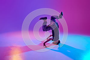 Stylish dressed young dancer, guy performing spinning on head in motion in mixed neon light against vibrant gradient