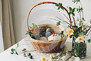 Stylish Easter basket with eggs and food with spring flowers on rustic table. Happy Easter! Traditional easter holiday food.