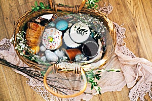 Stylish Easter basket with modern eggs, easter bread cake, ham, beets, sausage, butter and green branches on rustic fabric with