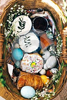 Stylish Easter basket with modern eggs, easter bread cake, ham, beets, sausage, butter and green branches on rustic fabric with