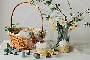 Stylish Easter bread, eggs and basket with food with spring flowers on rustic table. Happy Easter! Traditional easter holiday food