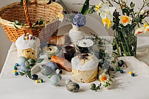 Stylish Easter eggs, bread and basket with spring flowers on rustic table. Happy Easter! Traditional easter holiday food for