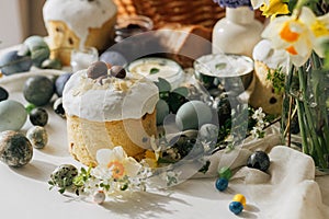 Stylish Easter eggs, bread and basket with spring flowers on rustic table. Happy Easter! Traditional easter holiday food for