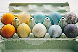 Stylish easter eggs in carton tray on white wooden background. Modern colorful easter eggs painted with natural dye in different