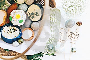 Stylish Easter eggs, easter bread cake, ham, beets, sausage, butter, green branches in wicker basket on white wooden background