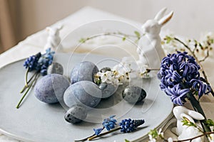 Stylish easter eggs on vintage plate, bunny and spring flowers on rustic table. Happy Easter! Natural dye blue eggs, purple