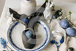 Stylish easter table setting. Easter egg in bunny napkin on vintage plate and spring flowers on rustic table. Happy Easter!