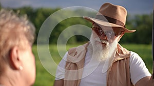 Stylish elderly gray-bearded gentleman in sunglasses and a brimmed hat looks at a notice on a pole about a missing dog