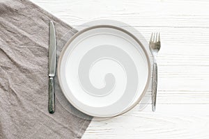 Stylish empty plate with vintage fork and knife on napkin on white table, flat lay. Modern set, serving for reception and