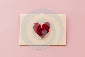 Stylish envelope with red heart flat lay on pink paper background. Modern valentine card, space for text. Happy Valentine`s day!