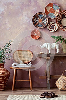 The stylish ethnic compostion at living room interior with wicker baskets, wooden bench, rattan chair and elegant personal