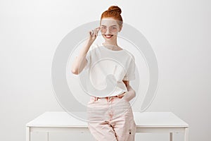 Stylish european ginger girl in trendy sunglasses standing and leaning on table, holding hand in pocket and gazing