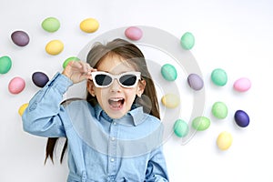 Stylish excited girl in dark sunglasses lies among the painted Easter eggs.