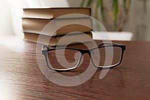 Stylish eyeglasses on office table on blurred background of stack of books