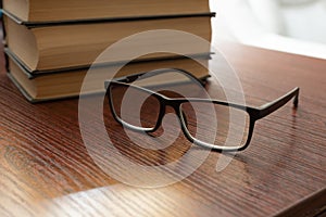 Stylish eyeglasses on office table on blurred background of stack of books