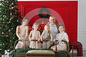 A stylish family with three children is sitting on a bed near a Christmas tree. A cozy Christmas holiday