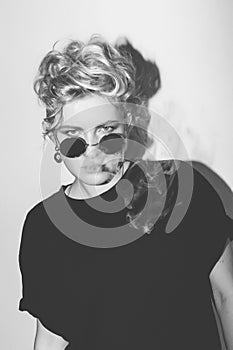 Stylish fashion blonde bad girl in a black t-shirt and rock sunglasses covered with cigarette smoke. Dangerous