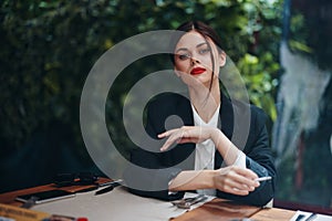 Stylish fashion woman sits in a cafe at a table and smokes a cigarette releasing smoke from her mouth with red lipstick