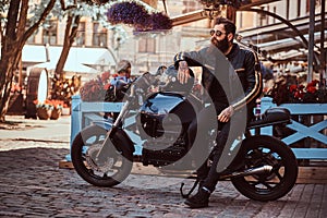 Stylish fashionable biker in sunglasses dressed in a black leather jacket, sitting on his custom-made retro motorcycle