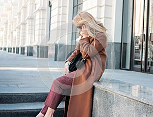 Stylish fashionable blonde woman wearing coat and sunglasses speaking on mobile phone, street style photo