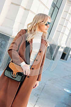 Stylish fashionable blonde woman wearing coat and sunglasses, street style photo