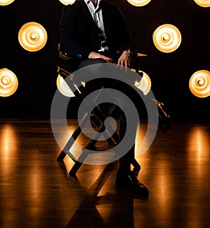 Stylish fashionable unrecognizable man sits on a chair in a jacket in a white shirt in a dark room with lamps