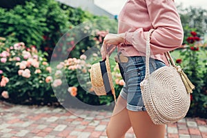 Stylish female handbag and straw hat. Young woman holding beautiful summer accessories outdoors. City fashion