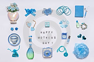 Stylish feminine accessories, flowers, cosmetics, jewelery, perfume in blue pastel colors on white background. Text HAPPY MOTHERS