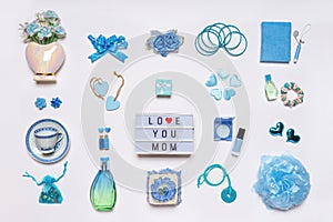 Stylish feminine accessories, flowers, cosmetics, jewelery, perfume in blue pastel colors on white background. Text LOVE YOU MOM