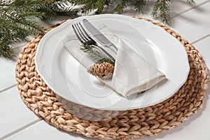 Stylish festive place setting with plate, cutlery and fir branches on white wooden table, closeup