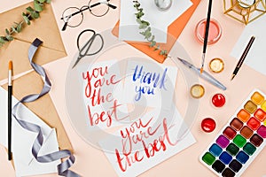 Stylish flatlay with art supplies, envelopes, brushes, watercolors, glasses, pen and a handmade cards