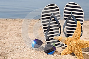 Stylish flip flops, sunglasses and starfish on sandy beach, space for text
