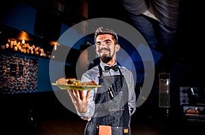 Stylish flunkey carries cooked dish on a black background.