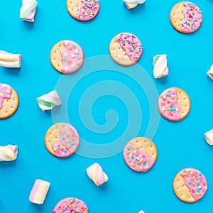 Stylish frame of cookies with pink glaze and marshmallow on blue background. Flat lay. top view.