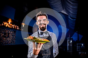 Stylish garcon serves dish on a black background.