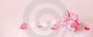 Stylish gift box with big pink bow and tender paper craft pink hearts on pink background, copy space, Greeting card, banner, flyer