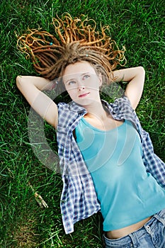 Stylish girl with dreadlocks lying on green grass