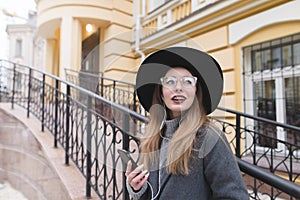 Stylish girl in a hat and glasses against the backdrop of old architecture. Happy girl with braces smiles sincerely