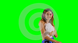 Stylish girl in headphones listens music and dance at green background