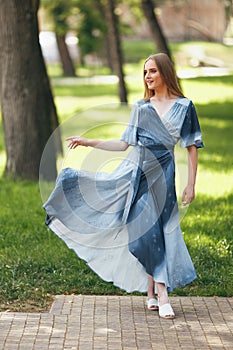 Stylish girl posing in a dress in a sunny spring park. Cheerful, happy portrait of a beautiful girl in the summer